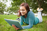 Happy casual student lying on grass using tablet