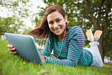 Cheerful casual student lying on grass using tablet