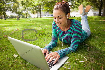 Smiling casual student lying on grass using laptop
