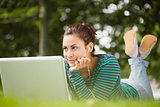 Thoughtful casual student lying on grass using laptop