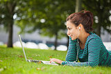 Attractive casual student lying on grass using laptop