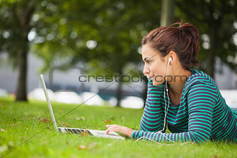 Attractive casual student lying on grass using laptop