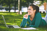 Laughing casual student lying on grass taking notes