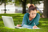 Calm casual student lying on grass taking notes