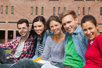 Five students sitting on the grass smiling at camera