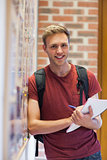 Handsome smiling student taking notes next to notice board