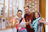 Three smiling students standing next to notice board showing thumbs up