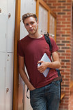 Handsome student leaning against lockers holding tablet