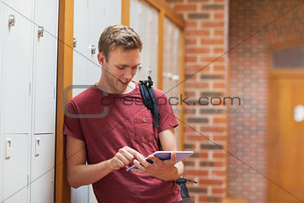 Handsome student leaning against lockers using tablet