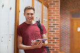 Handsome smiling student leaning against lockers using tablet