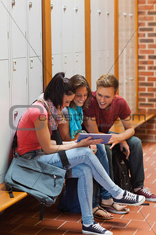 Smiling students sitting on bench using tablet
