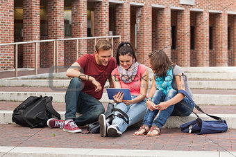 Smiling students sitting on stairs using tablet