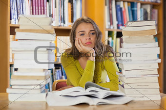 Thoughtful pretty student studying between piles of books