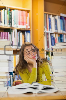 Exhausted beautiful student studying between piles of books