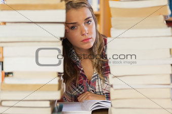 Stern pretty student studying between piles of books