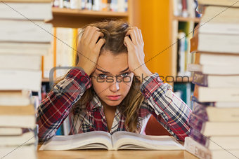 Annoyed pretty student studying between piles of books