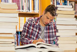 Focused handsome student studying between piles of books