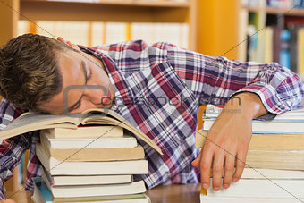 Tired handsome student resting head on piles of books