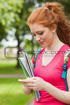 Gorgeous happy student holding notebooks texting