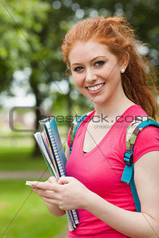 Gorgeous cheerful student holding notebooks texting