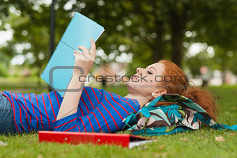 Gorgeous serious student lying on grass reading notes