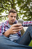 Handsome serious student sitting on grass texting