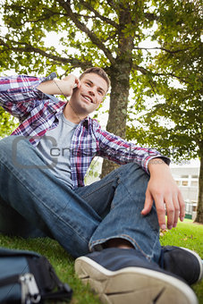 Handsome happy student sitting on grass phoning