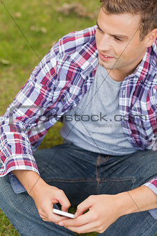 Handsome content student sitting on grass texting