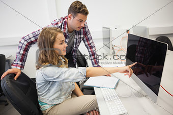 Two smiling students working on computer pointing at it