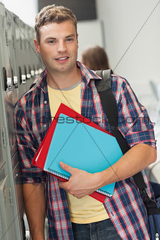 Happy handsome student standing next to locker