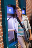 Pretty smiling student withdrawing cash smiling at camera