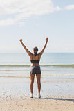 Rear view of slim young woman raising her arms standing on the beach
