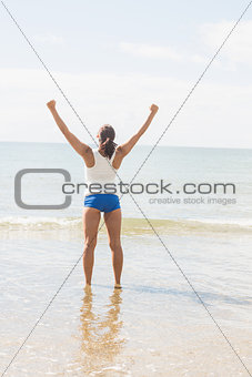 Rear view of slim young woman standing on the beach in bright sunshine