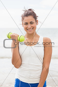 Cheerful smiling woman lifting dumbbells standing on beach