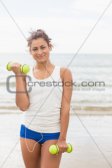Cute content woman lifting dumbbells on the beach
