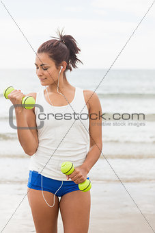 Focused smiling woman lifting dumbbells on the beach