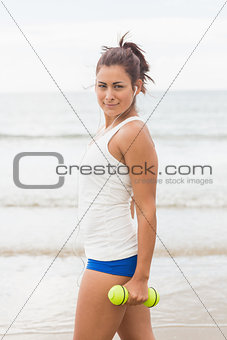 Lovely young woman holding dumbbells posing on the beach