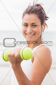Cute smiling woman lifting dumbbells on the beach