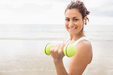 Smiling sporty woman lifting dumbbells on the beach