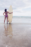 Slender woman in bikini with surfboard on beach