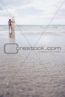 Calm woman in bikini with surfboard on beach
