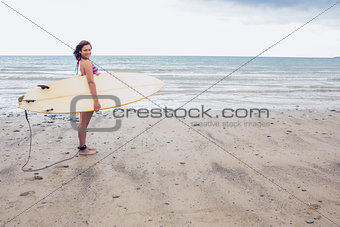 Smiling woman carrying surfboard on the beach