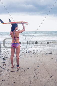 Bikini woman carrying surfboard on head at beach