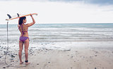 Bikini woman carrying surfboard on head at beach