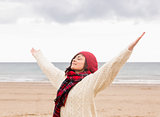 Woman in warm clothing stretching arms at beach