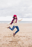 Woman in stylish warm clothing jumping at beach