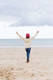 Woman in casual warm wear stretching arms on beach