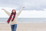 Woman in warm clothing stretching arms on beach