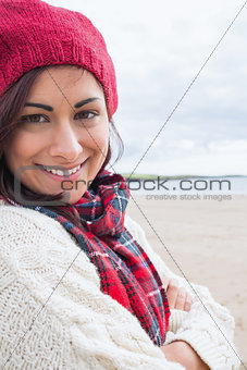Woman in knitted hat and pullover smiling at beach