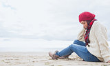 Woman in stylish warm clothing sitting at beach